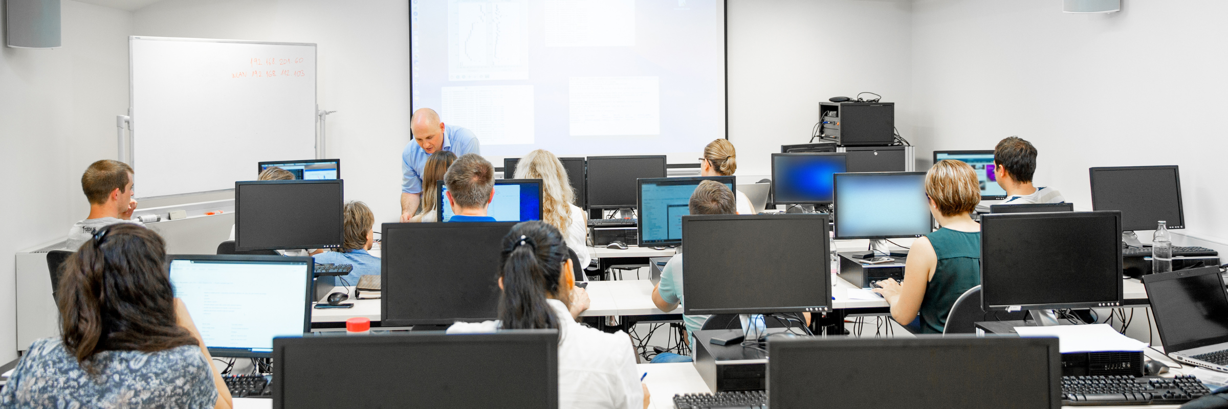 Interior of computer classroom with students being taught whilst sat around computers