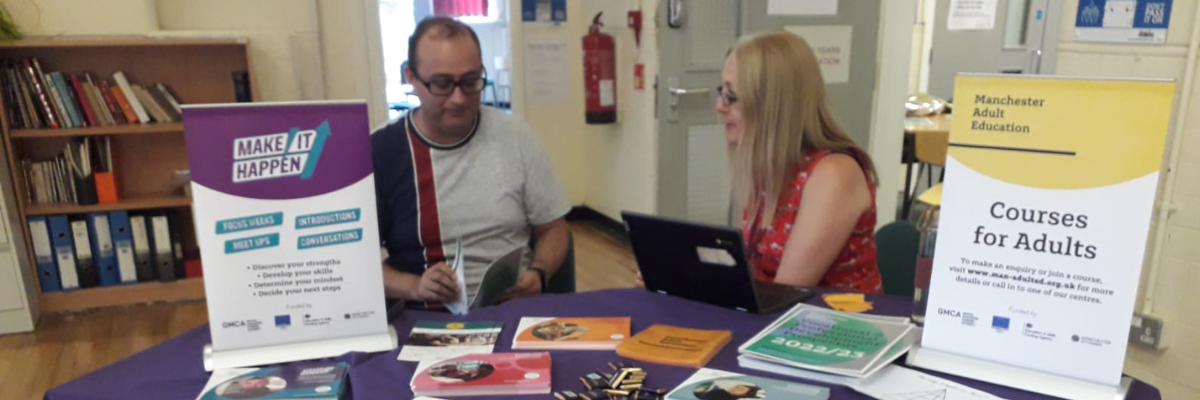 Two people sat at a table at an event with promotional material having a conversation