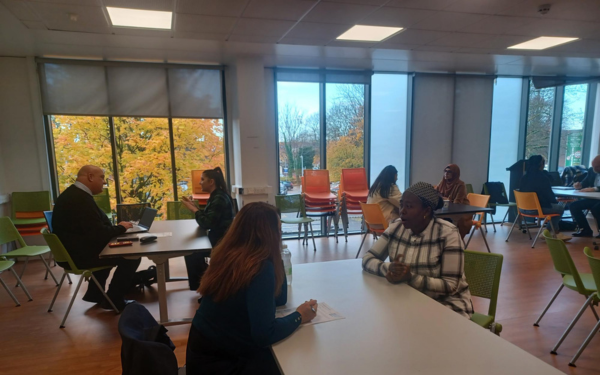People sat in groups of two at tables in a classroom doing a mock interview
