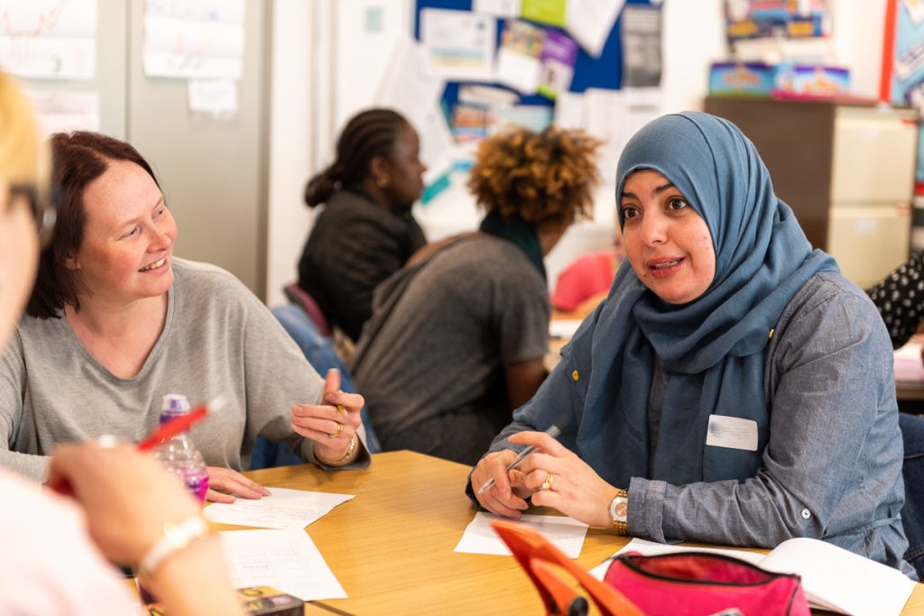 People sat around a table in a classroom laughing and listening to each other