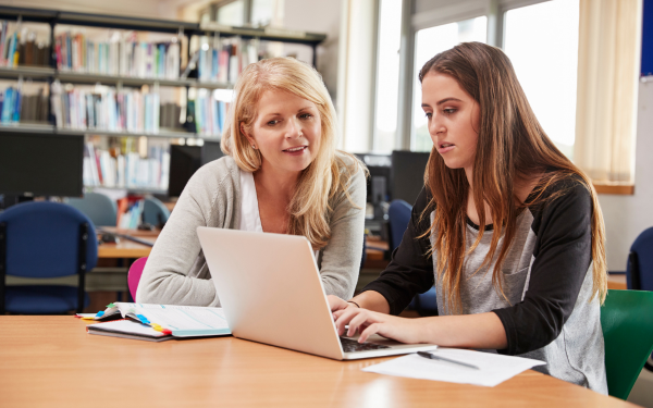 Two people sat at a library table working together on a laptop