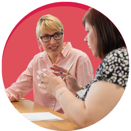 Image of two people sat having a conversation against a pink circle graphic background