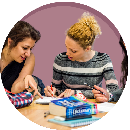 Two people sat at a table reading through a dictionary and making notes with a purple circle background