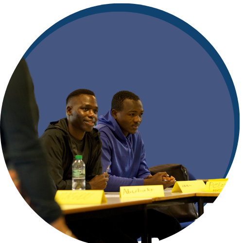 Two male learners sat at a desk in a classroom on a blue circle graphic background