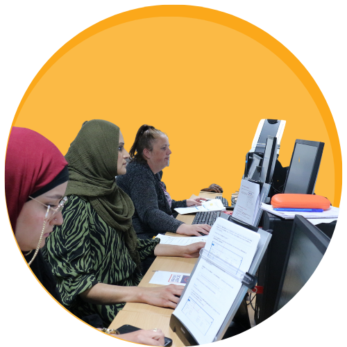 Women working at computers in a classroom on a orange cirlce background