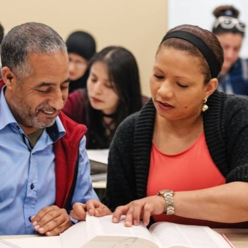A woman and man sat in a classroom reading a book together