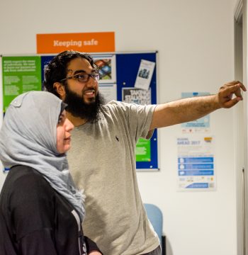 MAES-NB-4111 Two people pointing and looking at a noticeboard