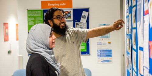 Two people pointing and looking at a noticeboard