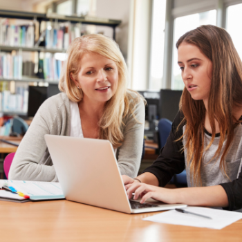 Two people sat at a library table working together on a laptop