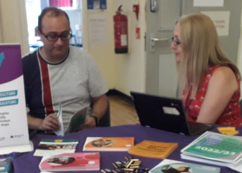 Two people sat at a table at an event with promotional material having a conversation