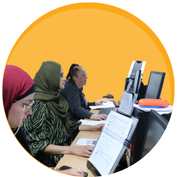 Women working at computers in a classroom on a orange cirlce background