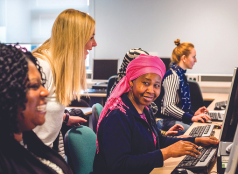 Several ladies on computers with a lady instructing them